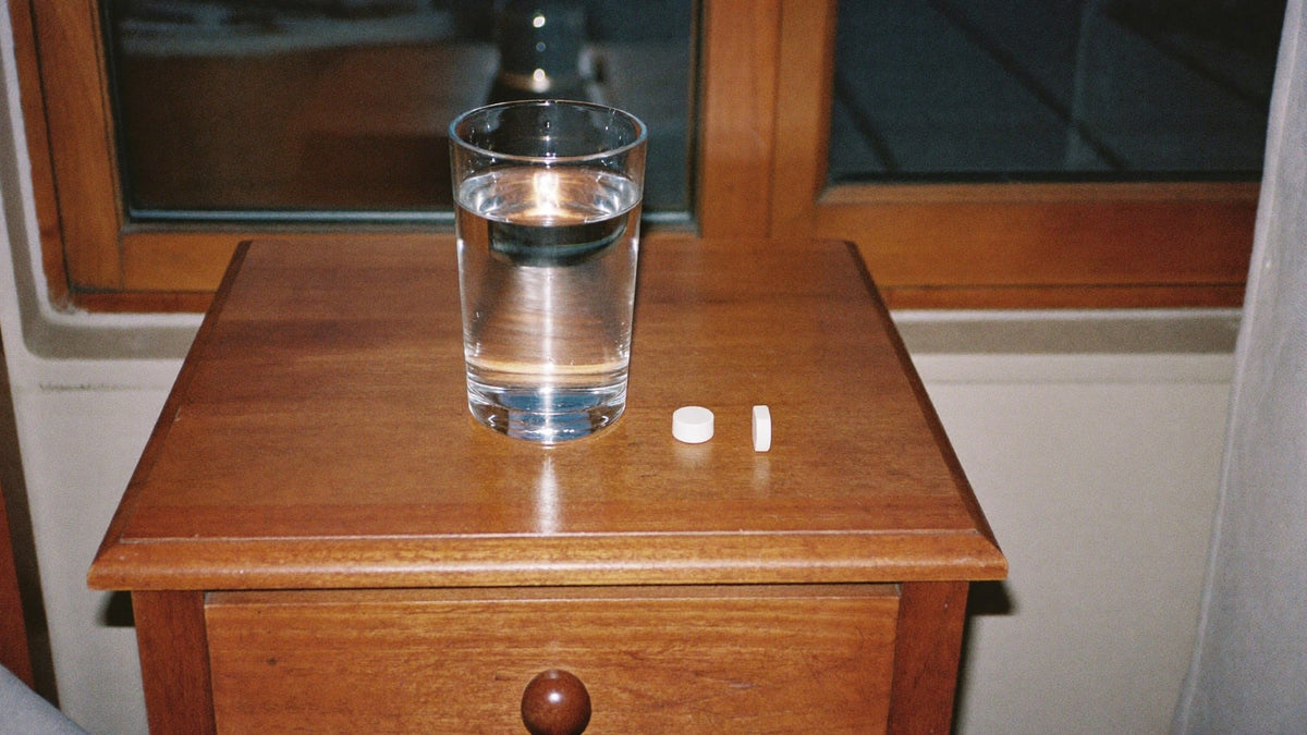 Glas Wasser und zwei Kapseln auf einem Nachttisch im Abendlicht